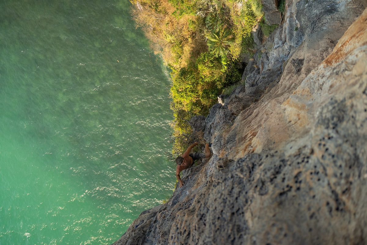 Climber on coastal limestone above turquoise water, Krabi